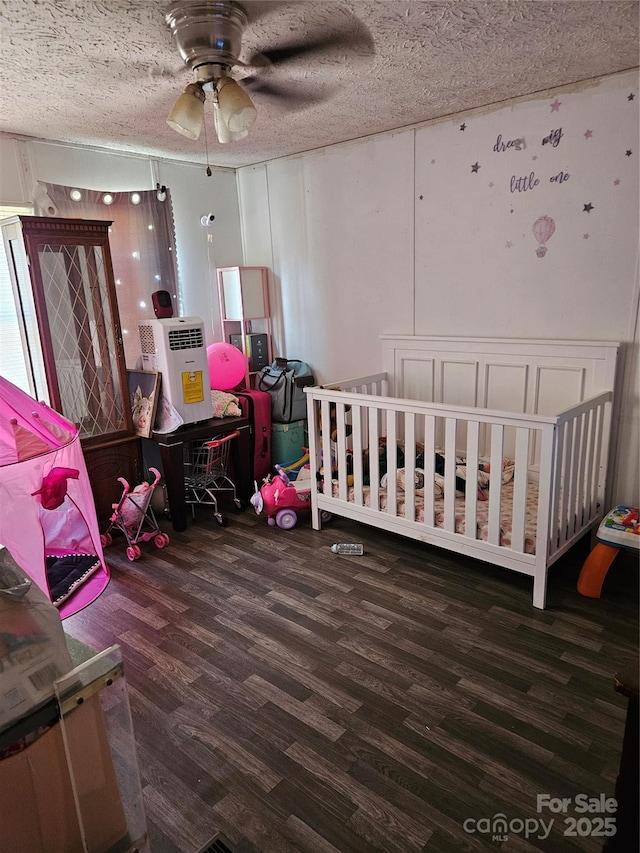 bedroom featuring a textured ceiling, ceiling fan, dark hardwood / wood-style flooring, and a nursery area