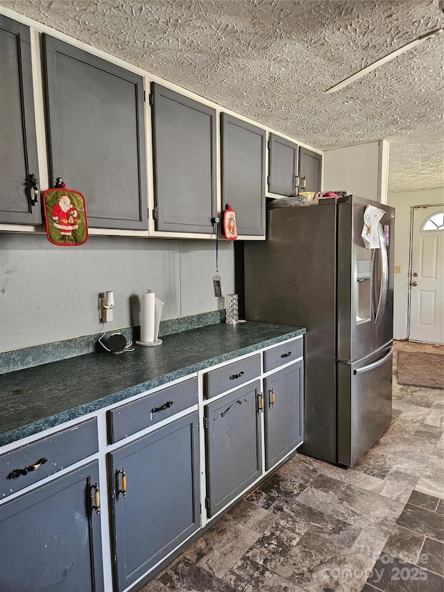 kitchen with stainless steel refrigerator with ice dispenser, gray cabinetry, and a textured ceiling