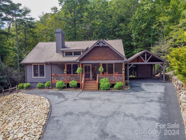 view of front facade featuring a forest view, a chimney, crawl space, a porch, and a carport