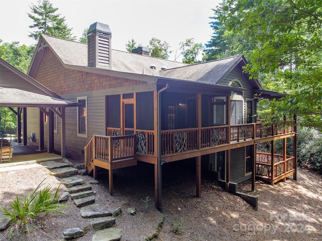 rear view of house featuring a shingled roof, a sunroom, a chimney, and a wooden deck