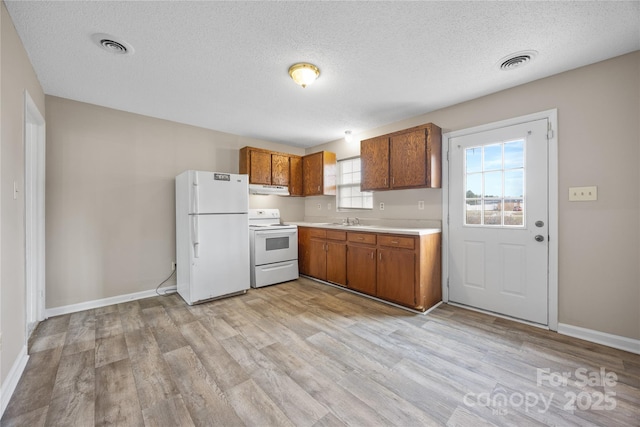 kitchen with light countertops, visible vents, brown cabinetry, a sink, and white appliances