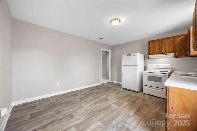 kitchen featuring white appliances, brown cabinets, light countertops, under cabinet range hood, and a sink