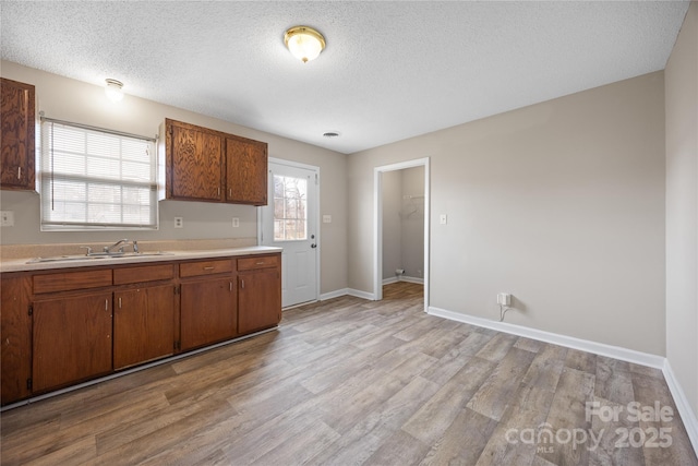 kitchen featuring light countertops, a sink, a textured ceiling, light wood-type flooring, and baseboards