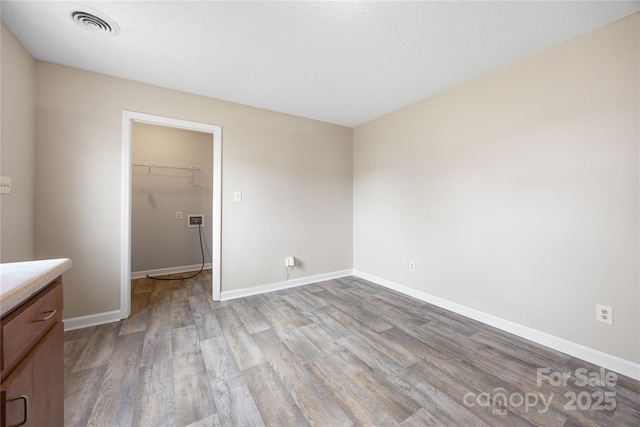 unfurnished bedroom featuring light wood-type flooring, baseboards, a spacious closet, and visible vents