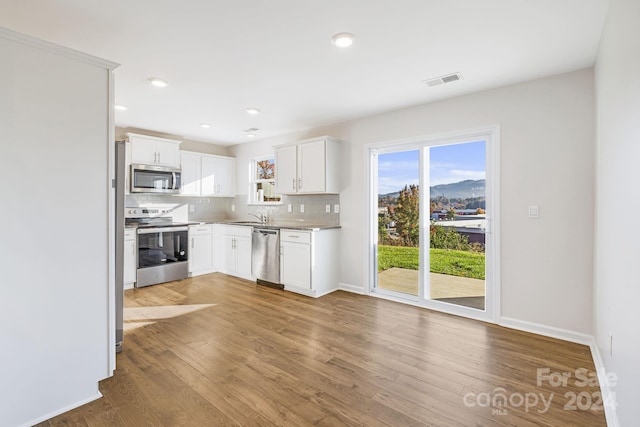 kitchen with tasteful backsplash, white cabinets, stainless steel appliances, and wood-type flooring