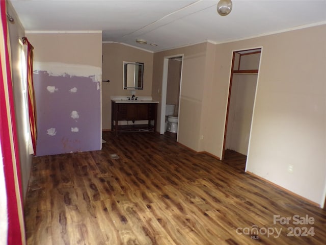 unfurnished bedroom featuring vaulted ceiling, ensuite bathroom, wood finished floors, and crown molding