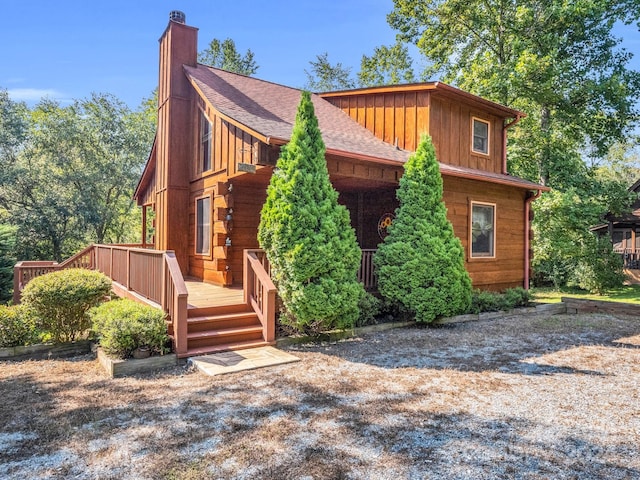 view of front of house with a shingled roof, a chimney, and a wooden deck