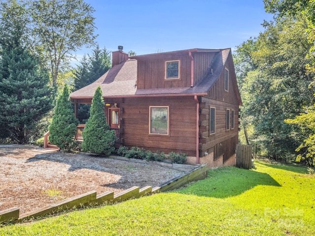 view of front of house with a shingled roof, a chimney, log siding, and a front lawn