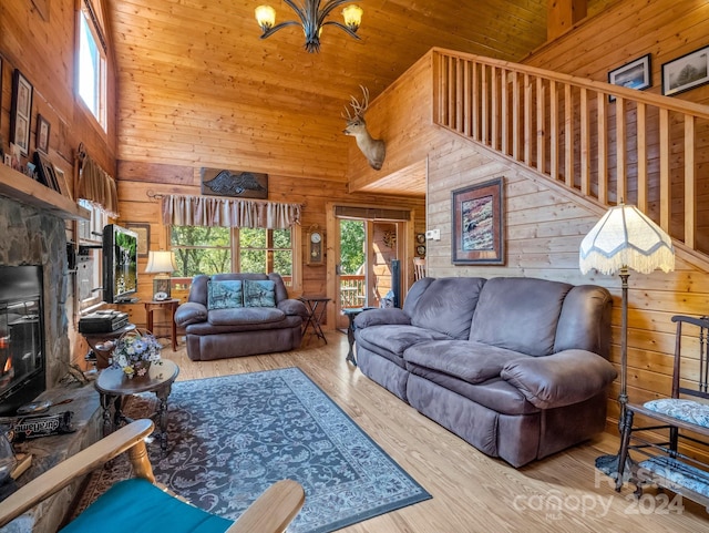 living room featuring a notable chandelier, a stone fireplace, wooden walls, wood finished floors, and stairs