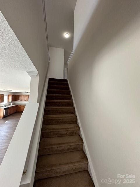 stairs featuring a textured ceiling, baseboards, and wood finished floors