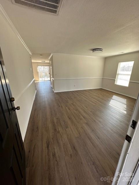 empty room with a textured ceiling, dark wood finished floors, visible vents, and baseboards