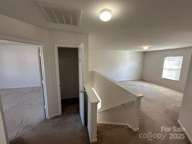 corridor featuring visible vents, dark carpet, a textured ceiling, and an upstairs landing