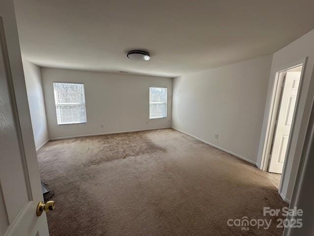 spare room with baseboards and light colored carpet