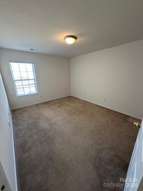 empty room featuring baseboards, dark colored carpet, and a textured ceiling