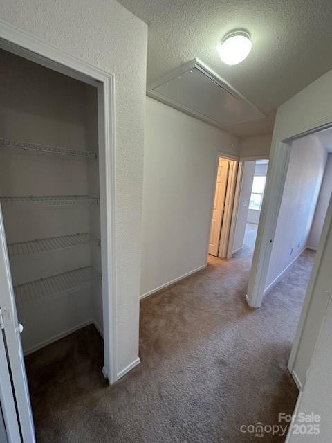 corridor with attic access, a textured wall, dark carpet, and a textured ceiling