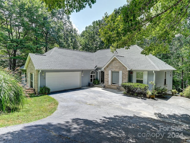 ranch-style house featuring an attached garage, driveway, a shingled roof, and brick siding