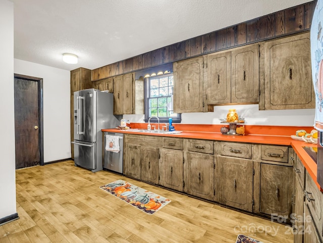 kitchen with light wood-type flooring, a textured ceiling, appliances with stainless steel finishes, and sink