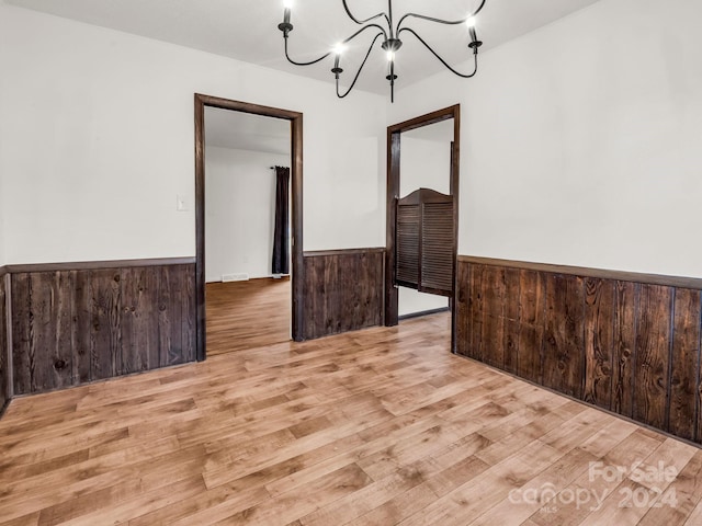 unfurnished room featuring an inviting chandelier, light wood-type flooring, and wood walls