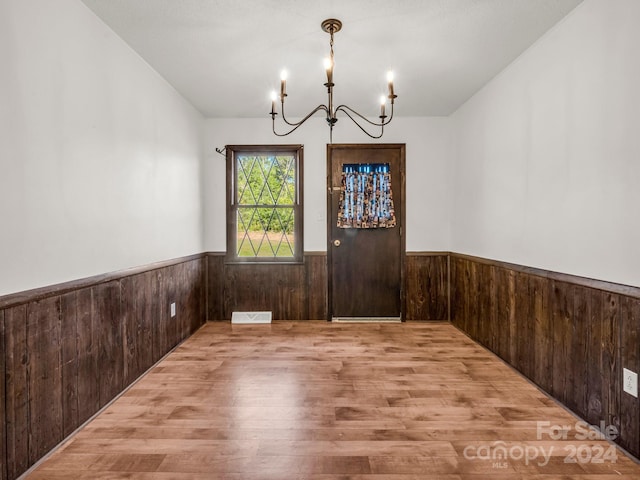 spare room with wood-type flooring, wooden walls, and a notable chandelier