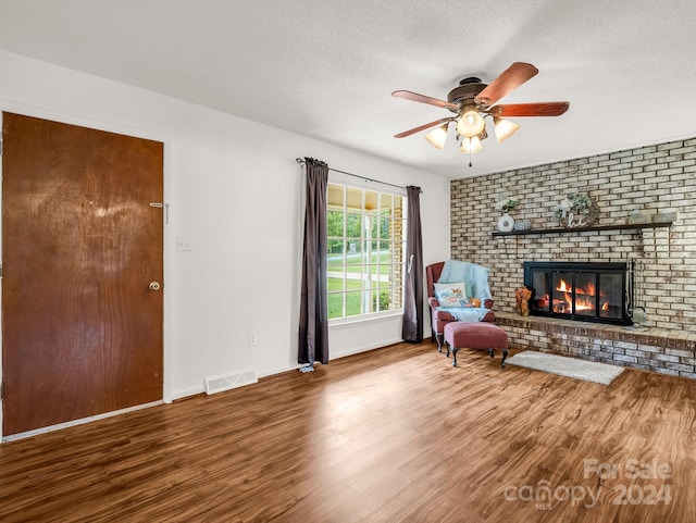 unfurnished room featuring a textured ceiling, hardwood / wood-style flooring, ceiling fan, and a brick fireplace