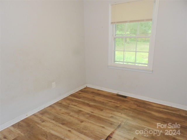 empty room with wood finished floors, visible vents, and baseboards