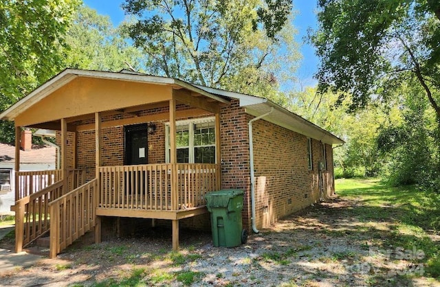 view of side of home with brick siding, crawl space, and a porch