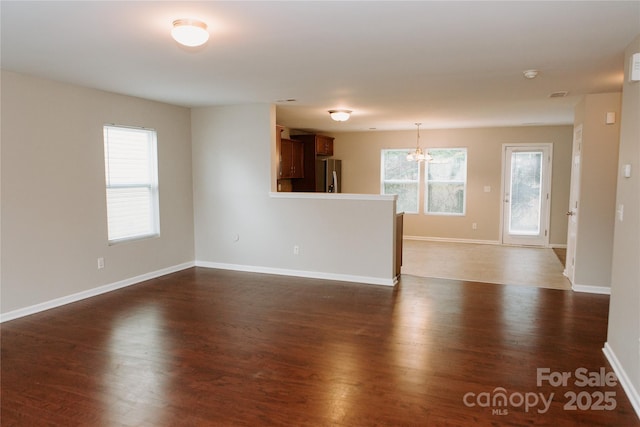 spare room with an inviting chandelier, dark wood-style floors, and baseboards
