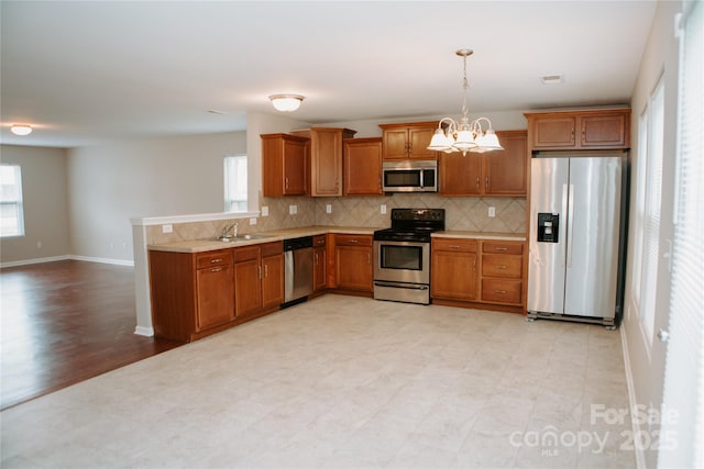 kitchen with light countertops, stainless steel appliances, decorative backsplash, a sink, and brown cabinets