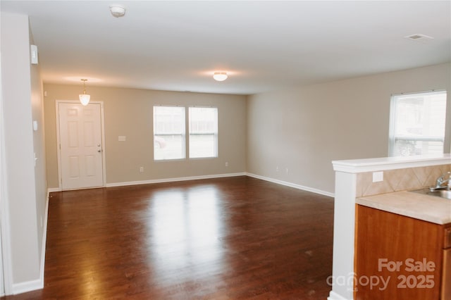 unfurnished living room with dark wood-type flooring, baseboards, a wealth of natural light, and visible vents