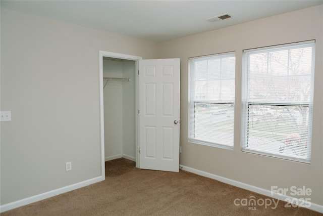 unfurnished bedroom with baseboards, visible vents, carpet floors, and a spacious closet