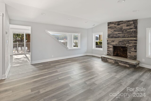 unfurnished living room with a fireplace, vaulted ceiling, and wood-type flooring