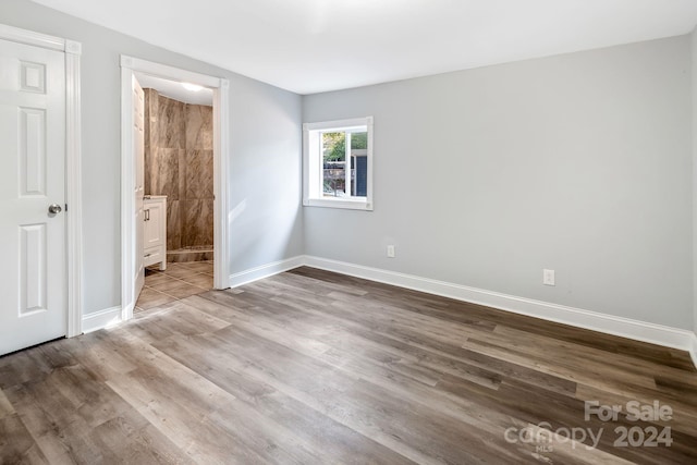 unfurnished bedroom with ensuite bath, baseboards, and wood finished floors