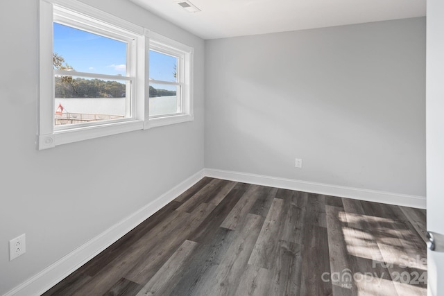 spare room with dark wood-type flooring, visible vents, and baseboards