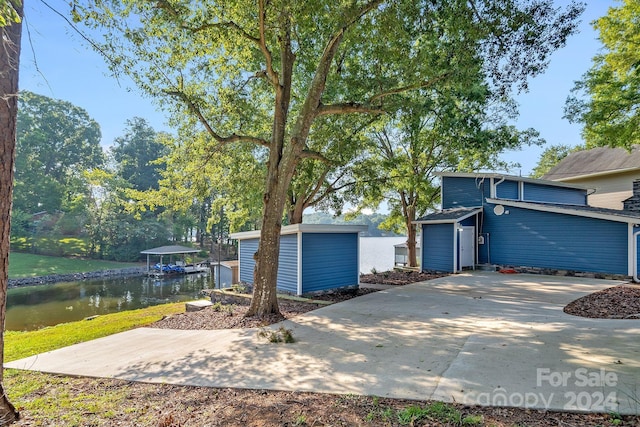 mid-century inspired home featuring a water view, a storage unit, concrete driveway, and an outbuilding