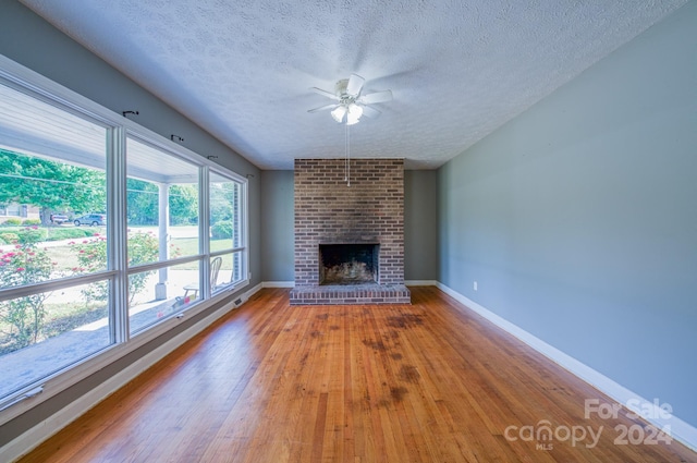 unfurnished living room featuring hardwood / wood-style floors, ceiling fan, a textured ceiling, and a brick fireplace