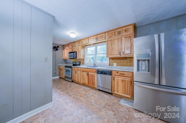 kitchen featuring a textured ceiling, stainless steel appliances, sink, and light stone countertops