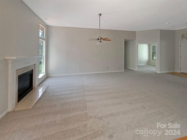 unfurnished living room with baseboards, a fireplace, a ceiling fan, and light colored carpet