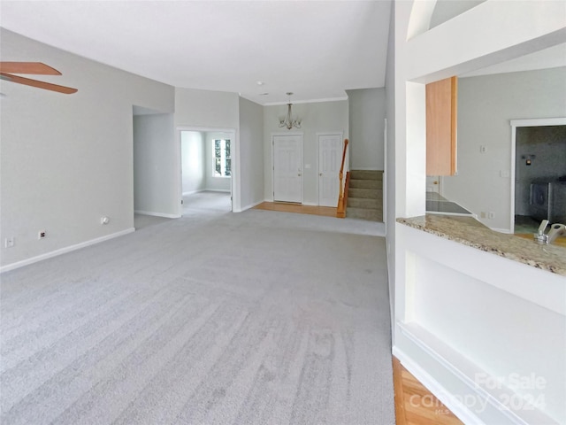 unfurnished living room featuring stairs, ceiling fan with notable chandelier, light carpet, and baseboards