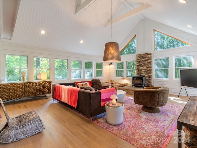 living room featuring light wood-type flooring, a wood stove, beamed ceiling, and plenty of natural light