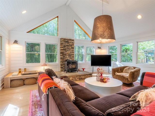 living room with a wealth of natural light, light hardwood / wood-style floors, high vaulted ceiling, and a wood stove