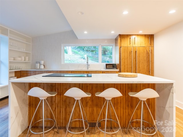 kitchen with black electric stovetop, lofted ceiling, light hardwood / wood-style flooring, and a kitchen bar