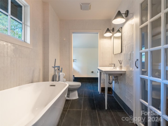 bathroom featuring tile walls, a tub, toilet, and tile patterned flooring