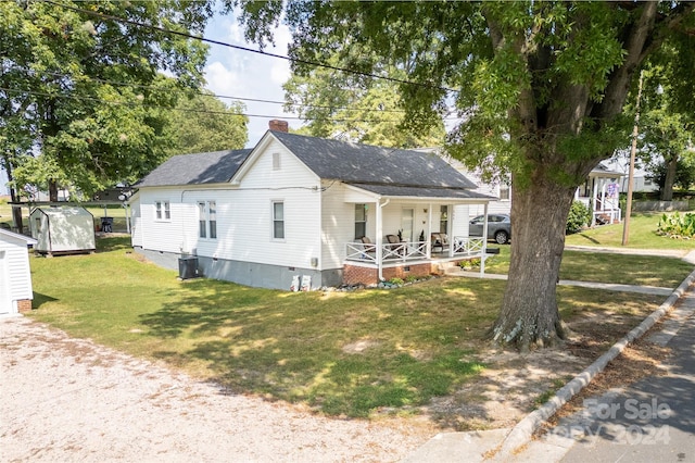 view of front of house featuring covered porch, central air condition unit, a shed, and a front lawn