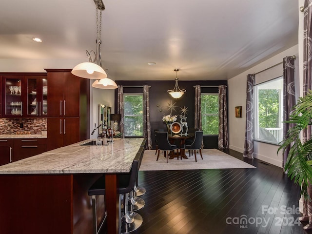 kitchen featuring sink, dark hardwood / wood-style floors, pendant lighting, tasteful backsplash, and a breakfast bar