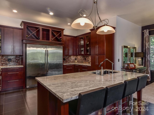 kitchen featuring backsplash, decorative light fixtures, light stone counters, built in fridge, and a sink