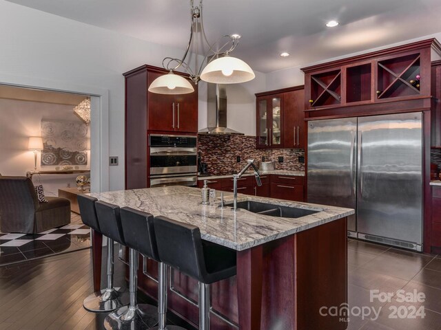 kitchen featuring appliances with stainless steel finishes, sink, wall chimney range hood, dark hardwood / wood-style floors, and a kitchen island with sink