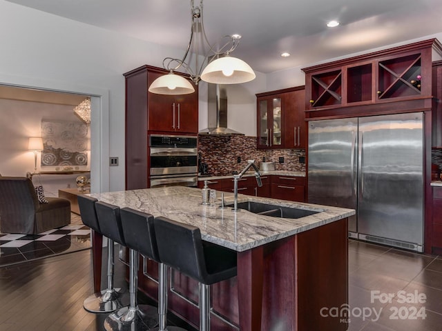 kitchen with wall chimney range hood, dark brown cabinets, appliances with stainless steel finishes, and a sink