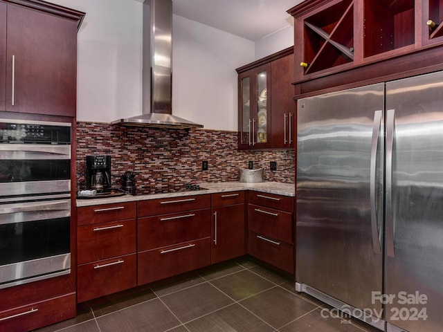 kitchen featuring dark tile patterned flooring, backsplash, stainless steel appliances, light stone countertops, and wall chimney exhaust hood