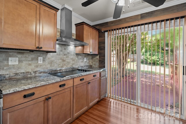 kitchen featuring light hardwood / wood-style flooring, light stone counters, wall chimney exhaust hood, black electric cooktop, and ceiling fan