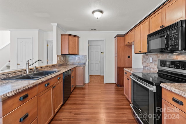 kitchen with black appliances, hardwood / wood-style floors, crown molding, sink, and decorative backsplash